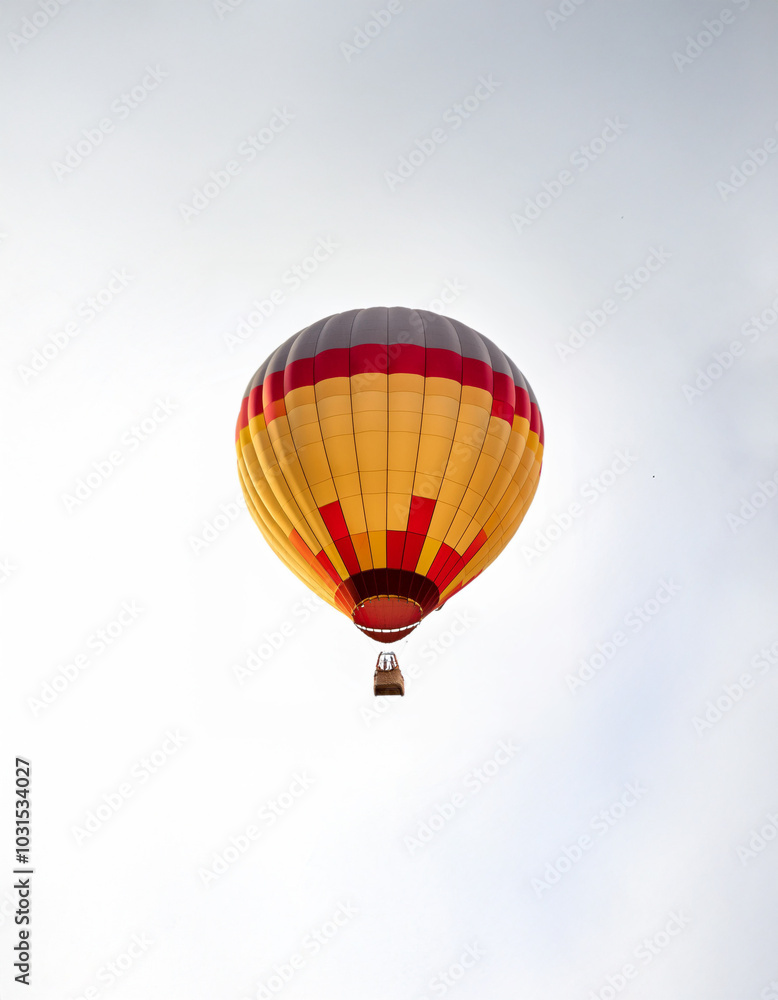 Fototapeta premium A red, yellow, and gray hot air balloon floats against a white sky.