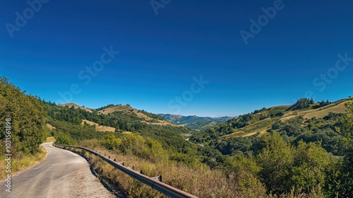 A winding road through a valley, with green hills and a clear blue sky.