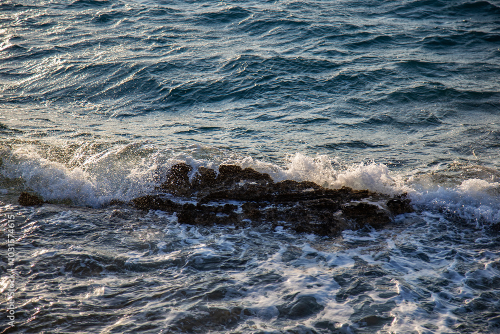 Obraz premium Waves crashing over a cluster of dark rocks, turbulent ocean