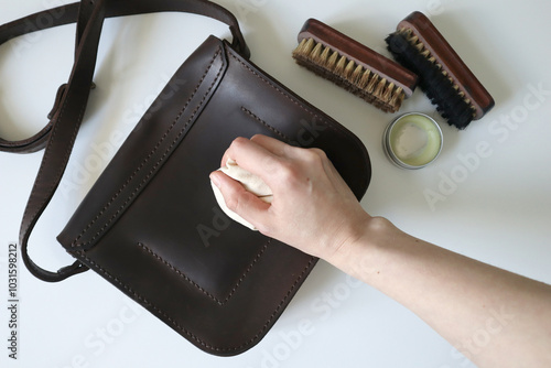 Photo process of cleaning leather products. Crazy horse leather bag. Human hand with a sponge. Brushes and wax are nearby. The bag is brown. White background. photo