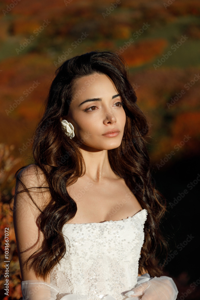 A woman in a white wedding dress stands on a hill before a forest A woman in a white wedding dress stands on a hill before a forest