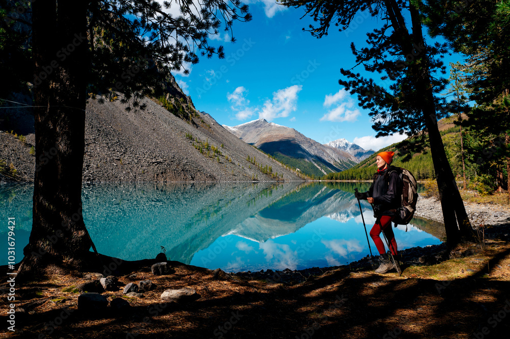 Fototapeta premium a tourist girl walks with a backpack along the shore of the mountain lake Shavlinskoye in autumn