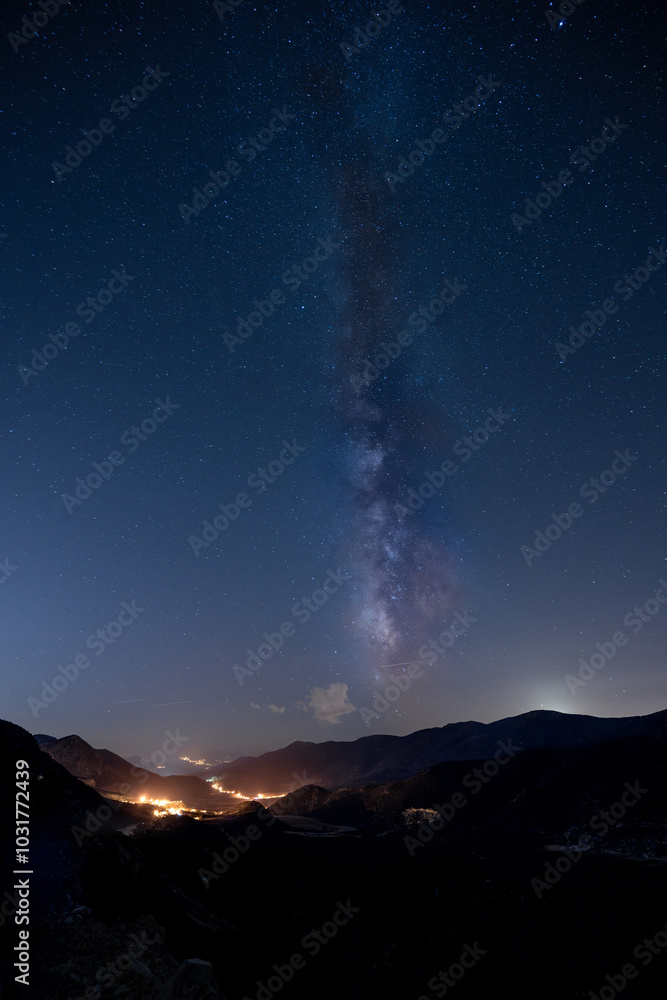 The Milky Way above the lights of a town in a valley The Milky Way above the lights of a town in a valley