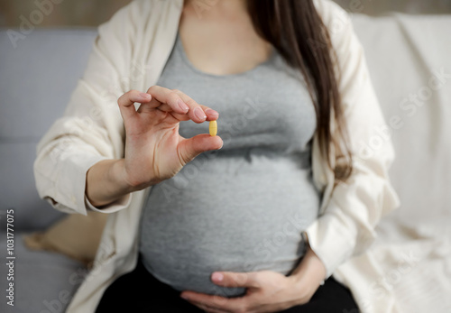Close up of young pregnant woman holding pill in hand, taking vitamins D, E, A, calcium, dietary supplements at home. Pregnancy, prenatal health and wellness, healthy nutrition, hydration