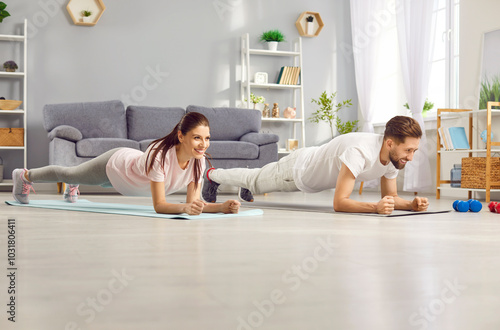 Fitness duo. Smiling man and woman are doing planks on yoga mats at home in spacious living room. Young couple who lead active and healthy lifestyle do sports together during home workouts.