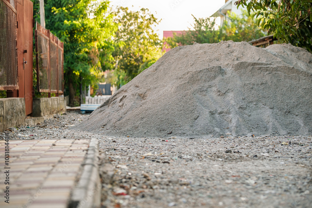 A significant mound of gravel sits on a gravel road in a suburban neighborhood, framed by greenery and residential buildings during the golden hour. A significant mound of gravel sits on a gravel road in a suburban neighborhood, framed by greenery and residential buildings during the golden hour.