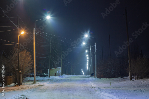 Evening village street illuminated by lampposts. Barancha, Ural, 2023.