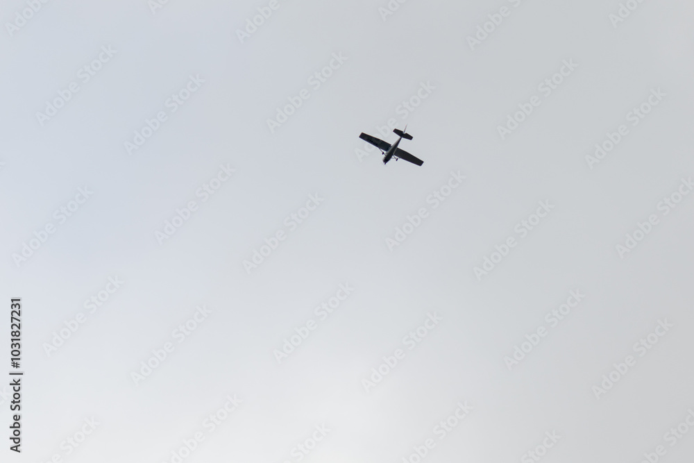 A small airplane flying overhead against a cloudy sky, viewed from below A small airplane flying overhead against a cloudy sky, viewed from below