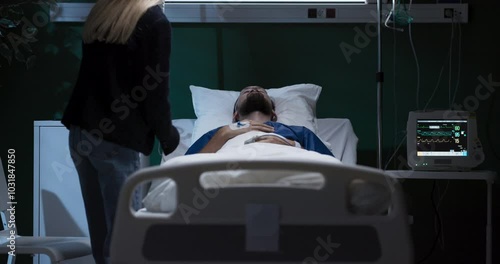 Exhausted tired young woman enters the hospital ward of his husband sits and supports while man in coma .