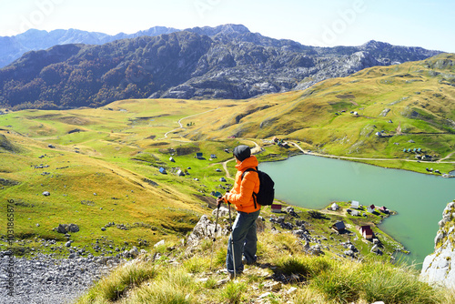 A tourist in a bright jacket stopped during the climb to the top to enjoy the beautiful panorama. A man traveling alone with a backpack against the backdrop of a mountain valley and Kapetanovo Lake photo