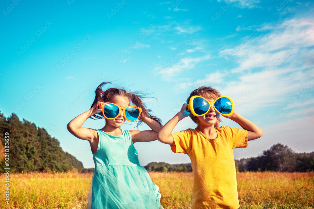 Happy little girl and boy with big funny sunglasses looking at the sun. The kids is in the countryside