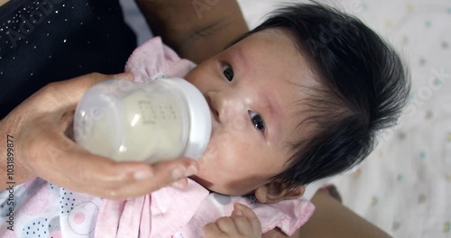 Baby girl receiving milk from a bottle, tenderly fed by her mother. A touching moment of care, promoting healthy growth, bonding, and the essentials of infant nutrition. photo