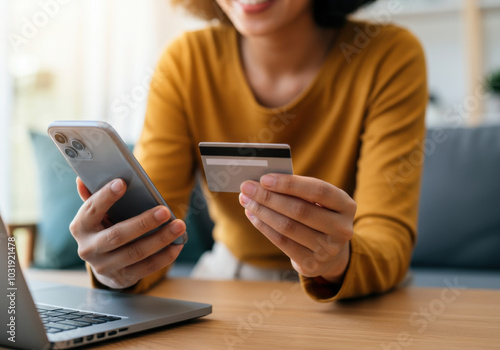 A woman using a smartphone and credit card for online shopping while sitting at a wooden desk