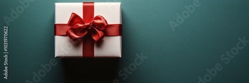 A beautifully wrapped white gift box with a red ribbon resting on a vibrant r...