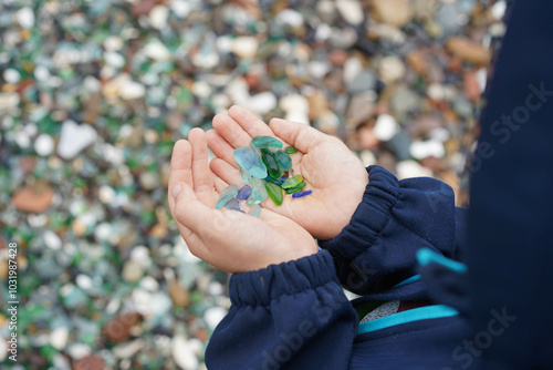 Rounded pieces of glass in the hands of a child on the beach, Vladivostok. Steklyannaya Bay, sand from pebbles, Far East, Primorsky region, Russia