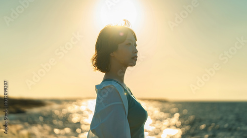 夕暮れの海辺にたたずむ女性