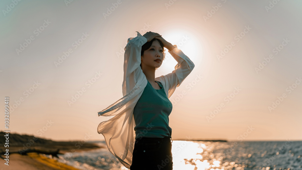 Fototapeta premium 夕暮れの海辺にたたずむ女性
