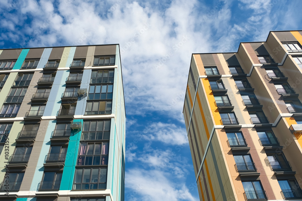 Apartment buildings against a bright blue sky with fluffy clouds in an urban setting during the daytime Apartment buildings against a bright blue sky with fluffy clouds in an urban setting during the daytime