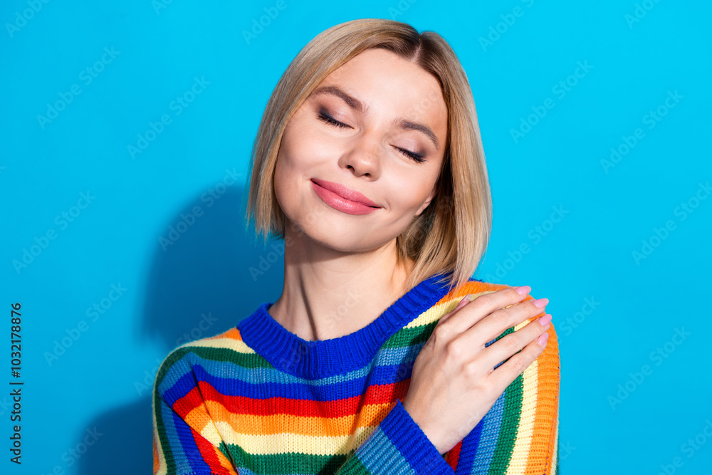 Photo portrait of lovely young lady hugging self closed eyes dressed stylish striped garment isolated on blue color background Photo portrait of lovely young lady hugging self closed eyes dressed stylish striped garment isolated on blue color background