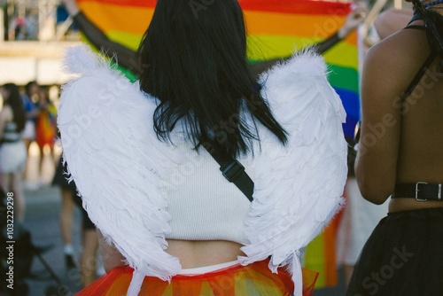 Young girl in angel costume with white wings back view. People in costumes at carnival, gay parade in summer. Youth festival. Multicoloured gay pride photo