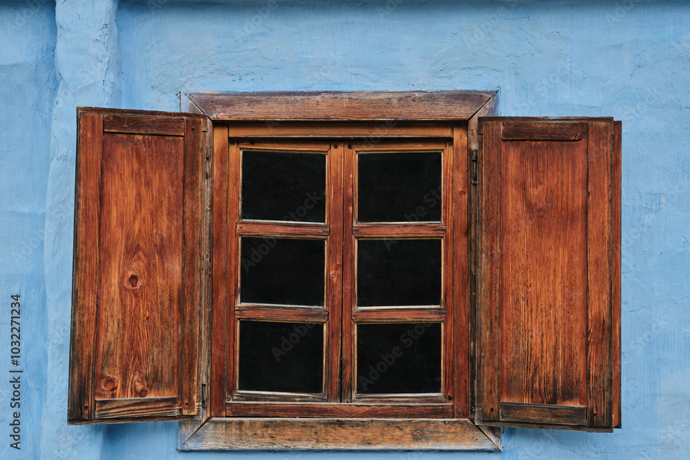 A rustic wooden window with shutters, framed against a faded blue wall. indow has multiple panes, creating a classic, vintage aesthetic. A rustic wooden window with shutters, framed against a faded blue wall. indow has multiple panes, creating a classic, vintage aesthetic.