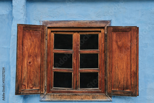 A rustic wooden window with shutters, framed against a faded blue wall. indow has multiple panes, creating a classic, vintage aesthetic.  photo