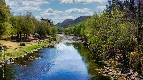 Landscape view of Santa Rosa river going trough Calamuchita small town. Large green trees in both sides photo