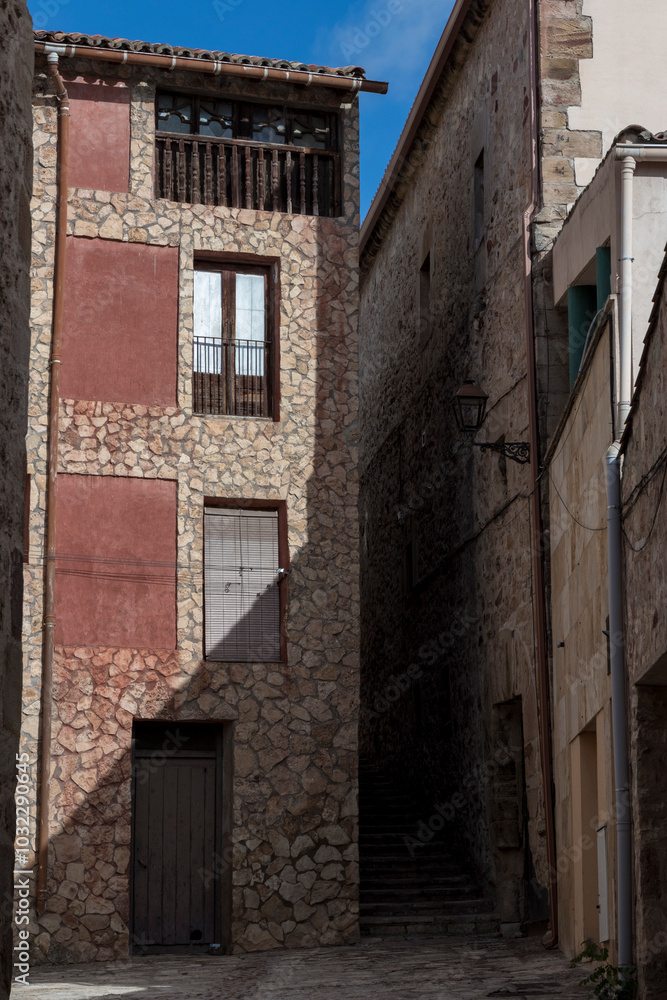 Narrow stone alleyway with rustic building facade and wooden door under a clear blue sky Narrow stone alleyway with rustic building facade and wooden door under a clear blue sky