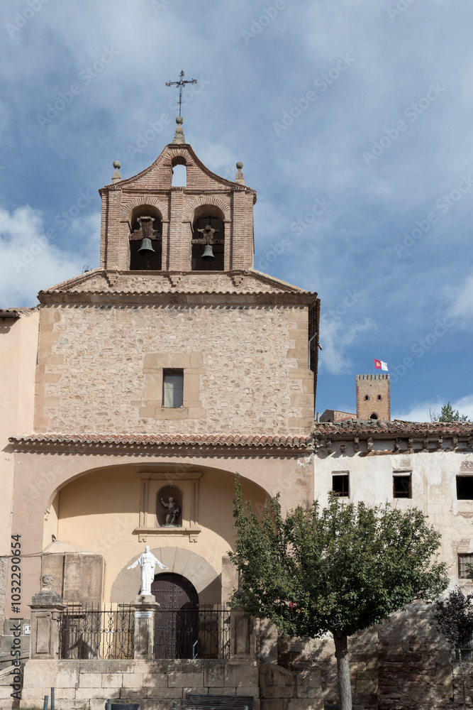 Fototapeta premium Historic church facade with bell tower and statue under a clear blue sky in a traditional village.