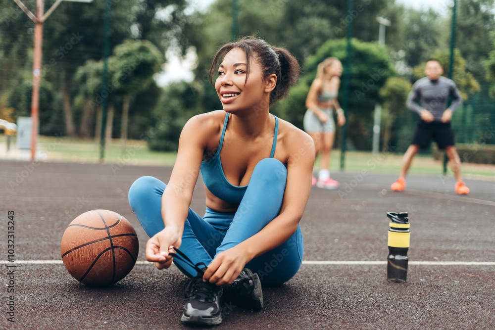 Smiling, African American woman tie shoelaces preparing playing basketball on the street, outdoors