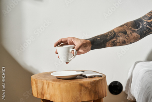 A young man with tattoos holding his coffee at home, surrounded by a relaxed atmosphere. photo