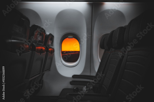 Wallpaper Mural View from an airplane window showcasing a stunning orange sunset on the horizon. The empty row of seats highlights the tranquility as the aircraft taxis on the runway, ready for takeoff. Torontodigital.ca
