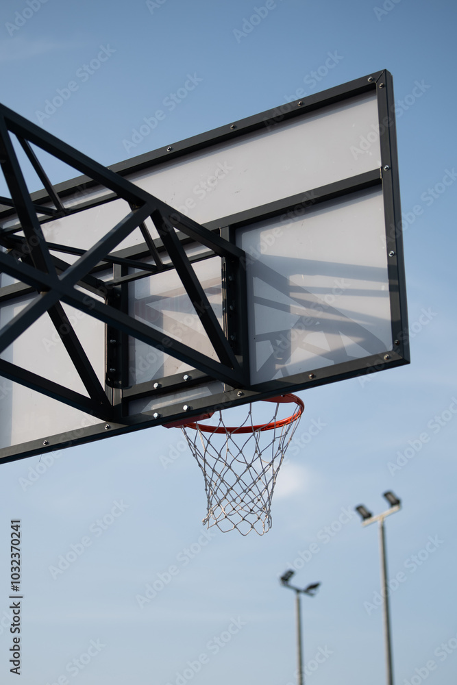 Basketball board with hoop outdoors on blue sky background.