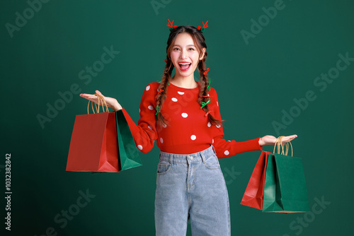 Young Beauty Asian happy woman wearing cozy red sweater dress and a reindeer antler hair clip carry shopping bags on green isolated background. winter, Happy new years concept. photo