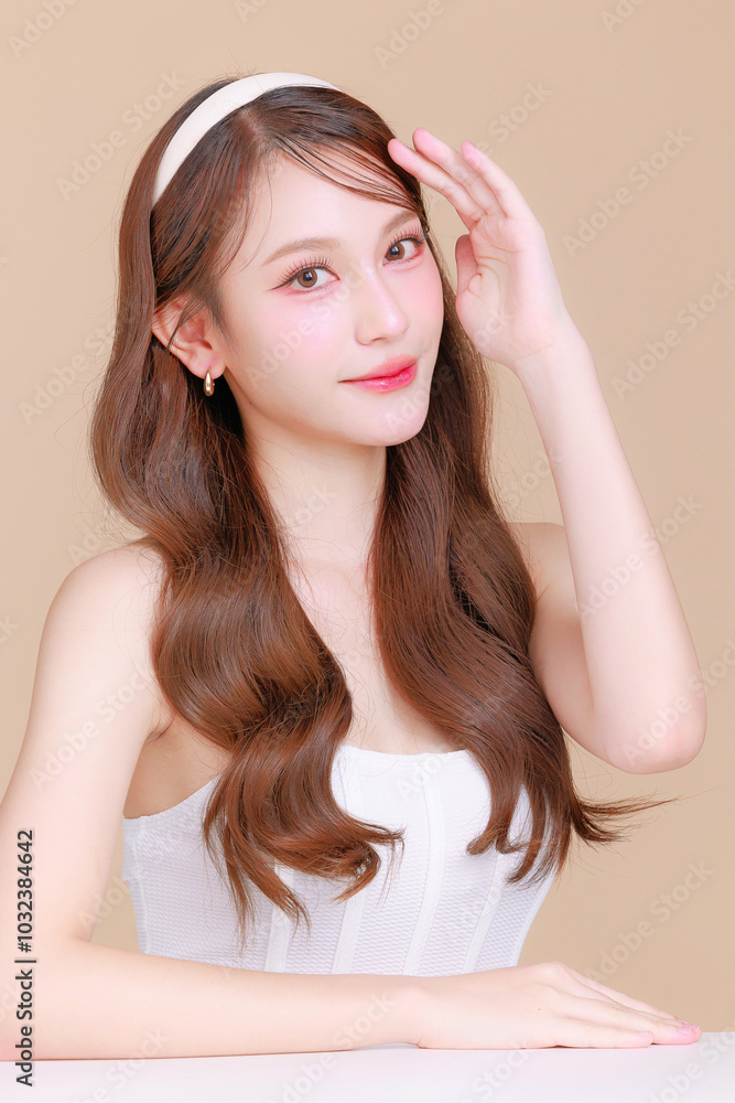 Pretty Asian beauty woman curly long hair with Korean makeup glowing face and healthy facial skin portrait smile on isolated beige background. Cosmetology ,Plastic surgery. Pretty Asian beauty woman curly long hair with Korean makeup glowing face and healthy facial skin portrait smile on isolated beige background. Cosmetology ,Plastic surgery.