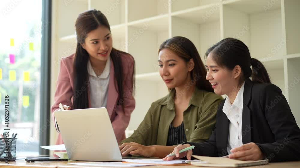 Three women in modern office engage in collaborative discussion while working on laptop, showcasing teamwork and professionalism among business professionals. Three women in modern office engage in collaborative discussion while working on laptop, showcasing teamwork and professionalism among business professionals.