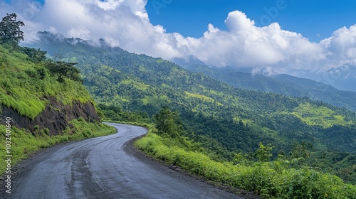 A winding road through lush green hills under a blue sky with clouds.