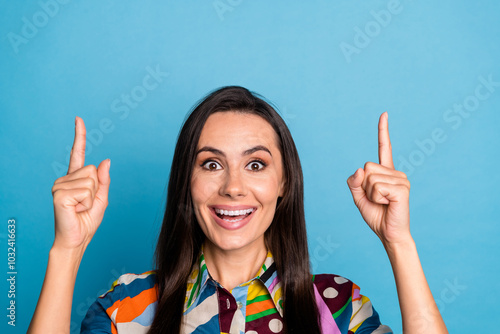 Photo portrait of lovely young lady point up excited empty space dressed stylish colorful print garment isolated on blue color background