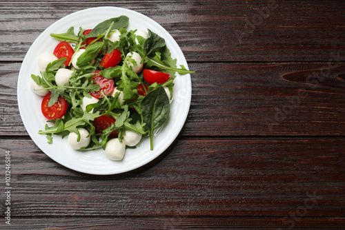 Tasty salad with arugula, spinach, mozzarella cheese and tomatoes on wooden table, top view. Space for text