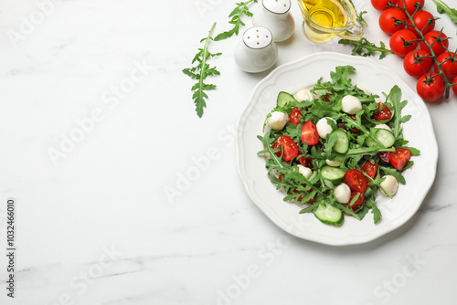 Tasty salad with arugula, mozzarella, tomatoes and cucumber on white marble table, flat lay. Space for text