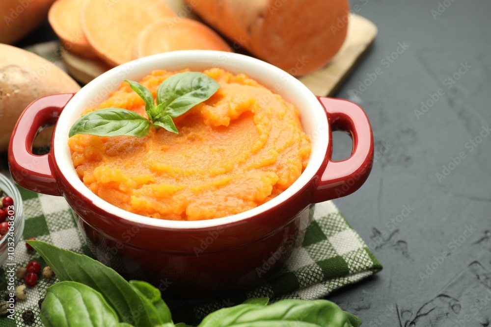 Tasty mashed sweet potato with basil in pot and fresh vegetables on dark textured table, closeup Tasty mashed sweet potato with basil in pot and fresh vegetables on dark textured table, closeup