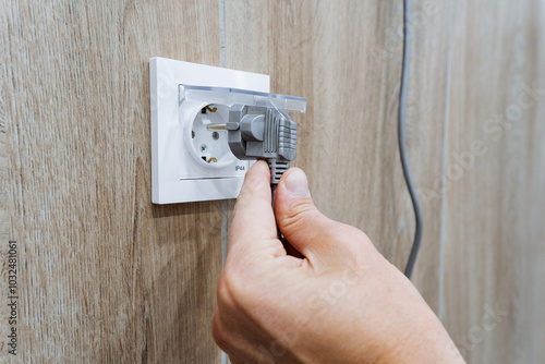 A diligent individual is meticulously focusing on inserting an electrical plug into the nearest available outlet to guarantee a secure and reliable power connection for their devices and equipment photo