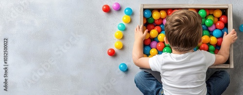 Child playing with colorful balls in a wooden box on a gray background.