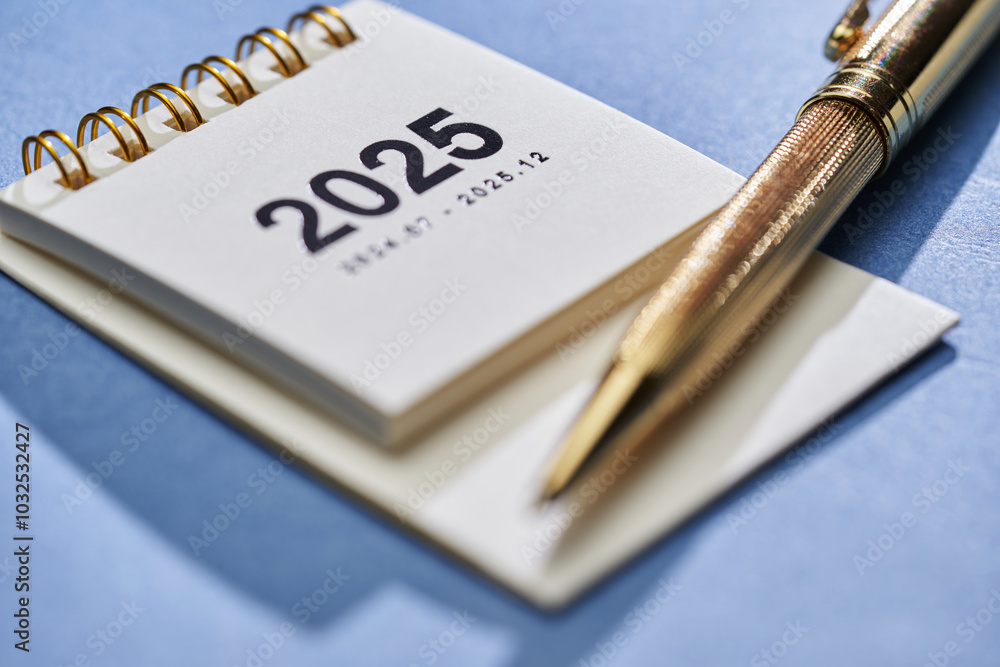 small 2025 desktop calendar with pen on blue background small 2025 desktop calendar with pen on blue background