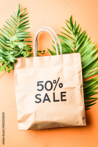 Advertisement for a 50 percent discount or rebate on a paper shopping bag with green leaves on a peach background. Winter sales concept.