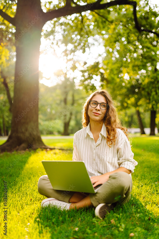 Young Woman sitting on green grass ground, working on laptop in city park. Mobile Office. Concept for education, business, blog or freelance. Young Woman sitting on green grass ground, working on laptop in city park. Mobile Office. Concept for education, business, blog or freelance.