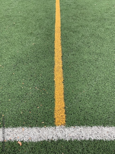 A centered view of a sports field showcasing two parallel lines: a vibrant yellow line running vertically and a bright white line running horizontally across green artificial turf.