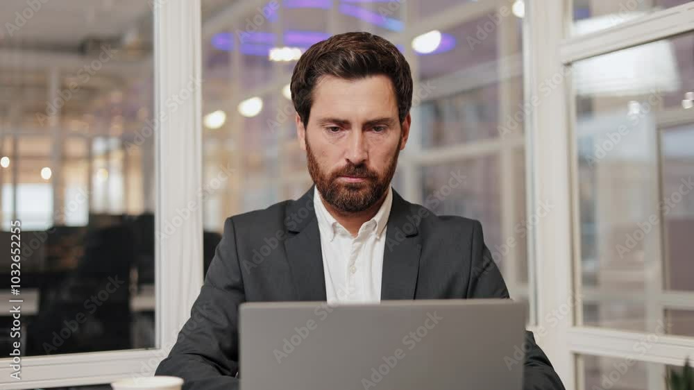 A businessman sits in a modern office, using a laptop and thinking of work solutions, strategy and progress. Slow motion shot. A businessman sits in a modern office, using a laptop and thinking of work solutions, strategy and progress. Slow motion shot.