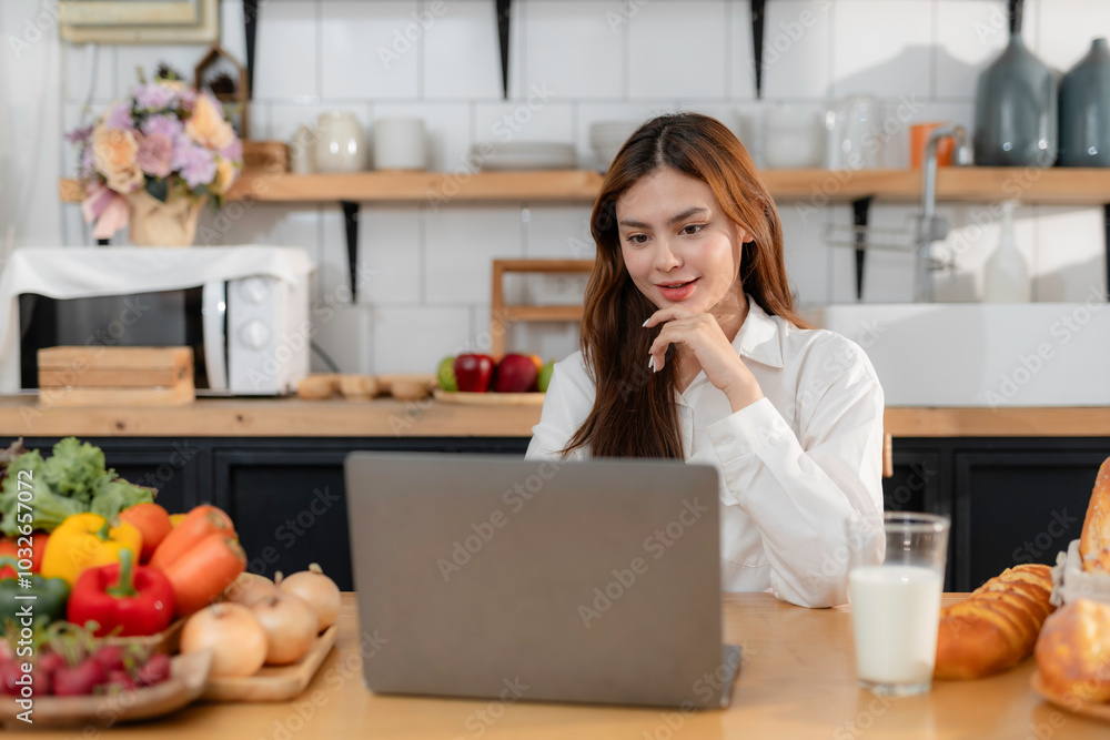 Young woman is using laptop, watching online cooking course and learning to prepare healthy food in her kitchen Young woman is using laptop, watching online cooking course and learning to prepare healthy food in her kitchen