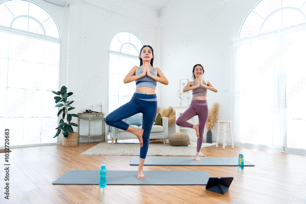 Obraz premium Couple Asian women exercise together with yoga posture by stand and hands together also stay on mat in room with day light.